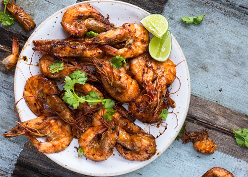 BBQ grilled prawns on a plate with lime wedges and coriander leaves